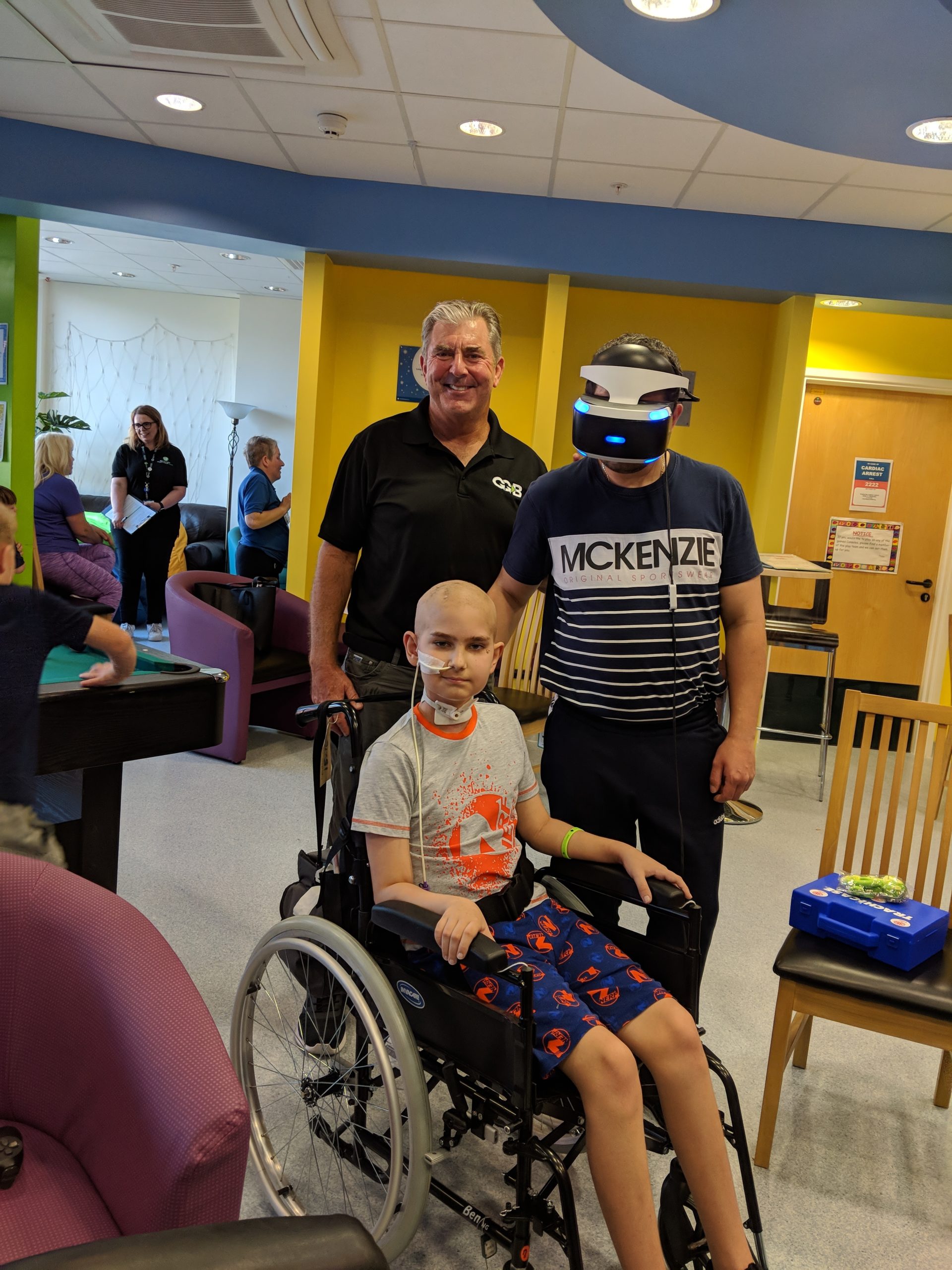 A young hospital patient and his dad sharing a VR headset in a hospital game room