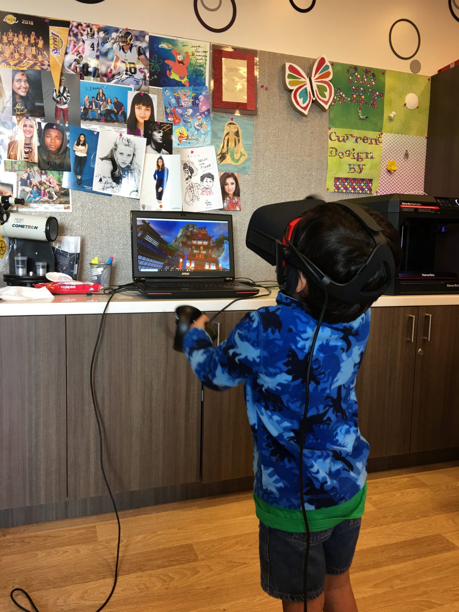 A child in a hospital playroom, immersed in a VR game with controllers raised — joy, not pity